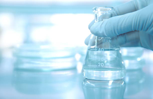 scientist-hand-in-rubber-glove-holding-clear-flask-with-blur-petri-picture-id817472086.jpg